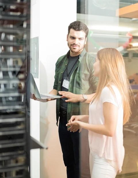 IT engineer holding a laptop while discussing server infrastructure with a colleague