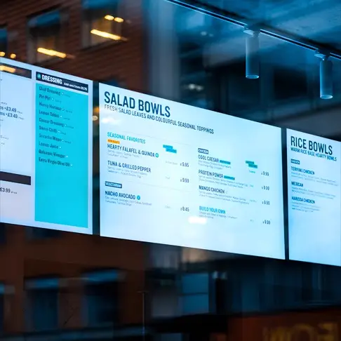 Digital menu boards displaying salad bowls and rice bowls in a restaurant